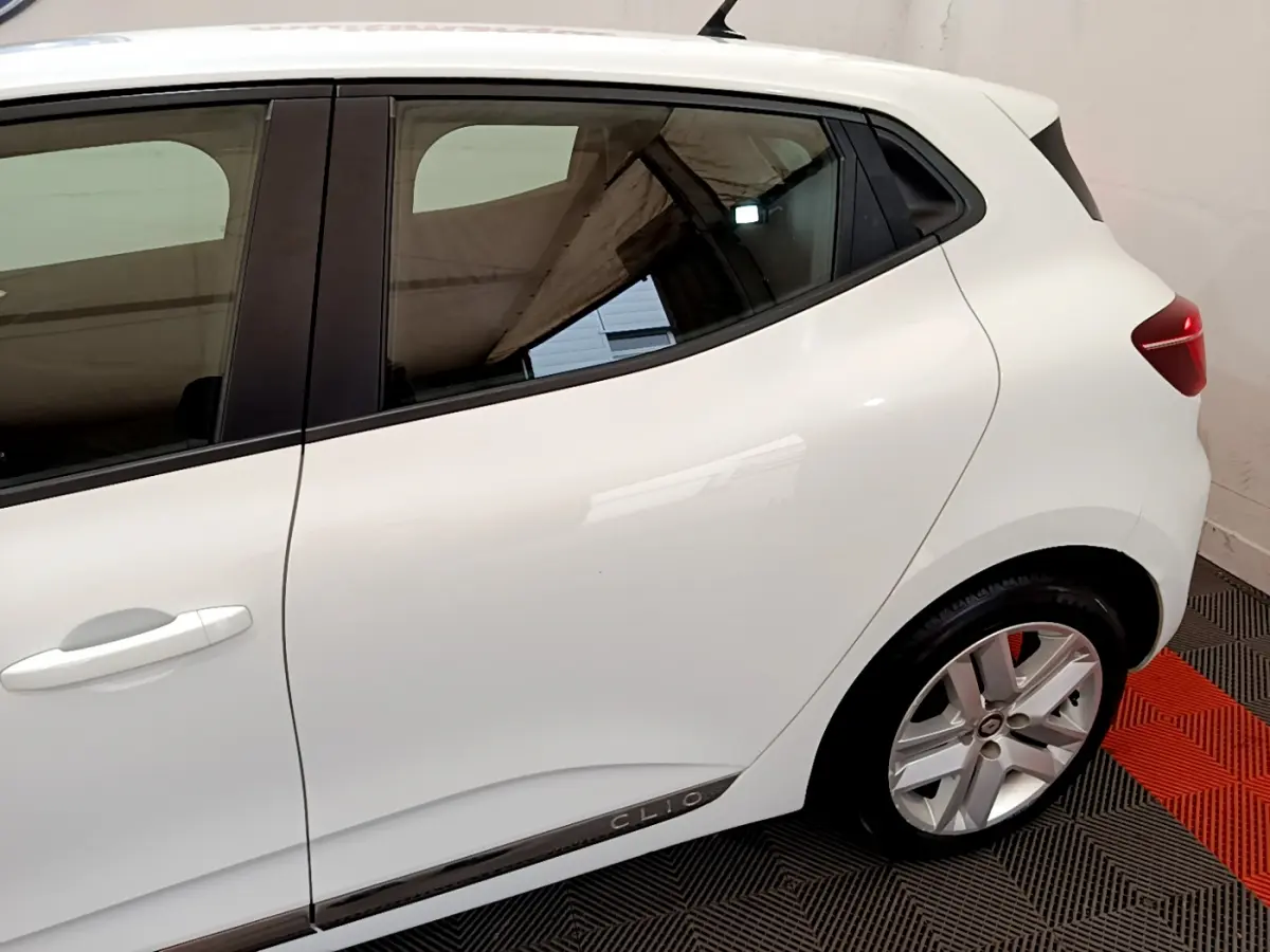 Vue côté droit arrière d'une Renault Clio Business blanche avec jante alliage et logo Clio sur la bas de porte.