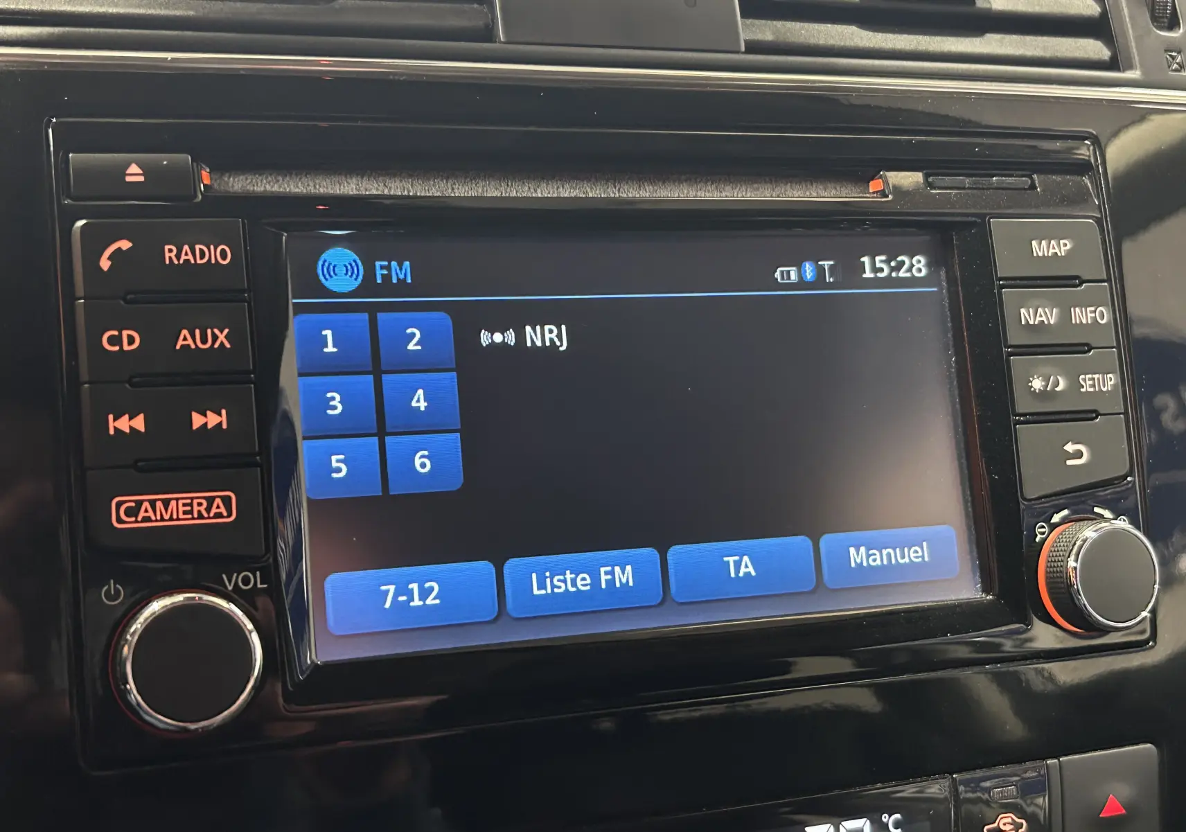 Gros plan sur l'écran multimédia noir de la Nissan Pulsar 2018 affichant la radio FM sur NRJ avec commandes tactiles et boutons physiques.