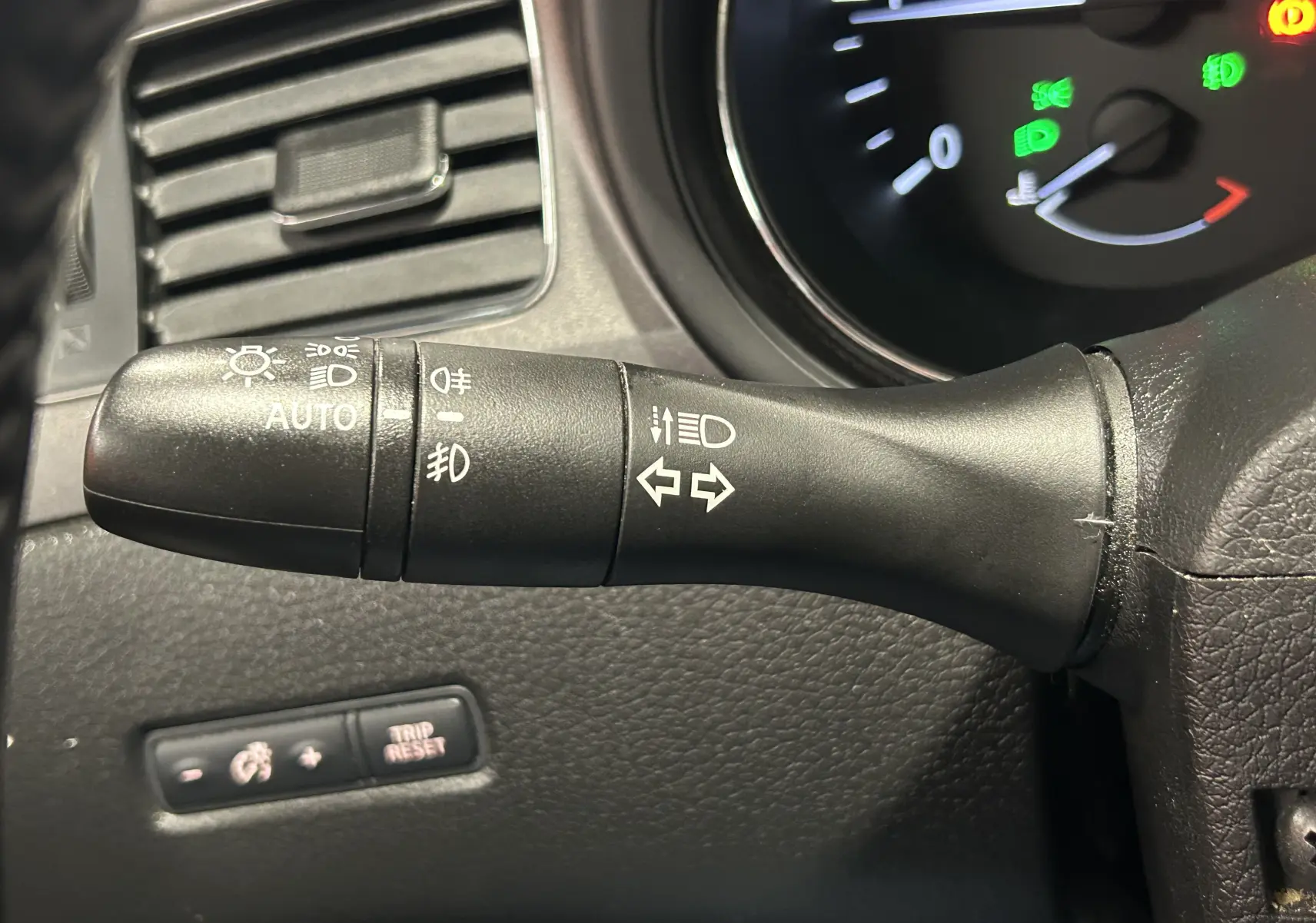 Gros plan sur la manette de commande des feux et clignotants à gauche du volant dans l’habitacle noir d’une Nissan Pulsar gris 2018.