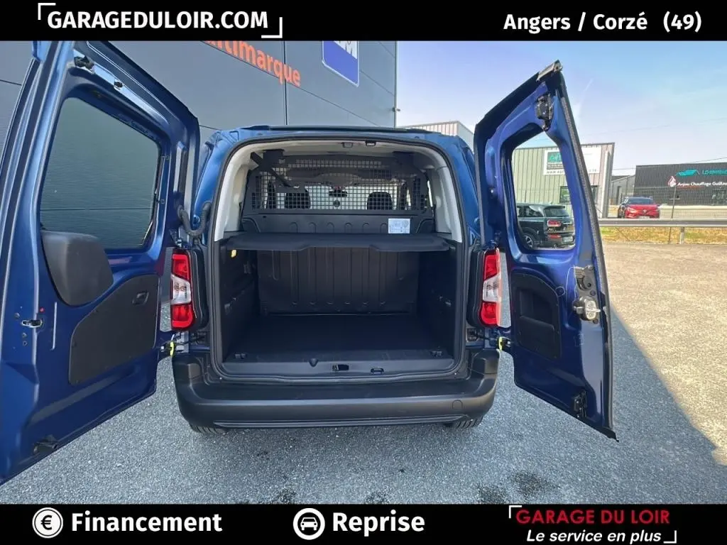 Vue arrière du Peugeot Rifter bleu 2024 avec portes ouvertes, montrant l’espace de chargement et la grille de séparation intérieure.