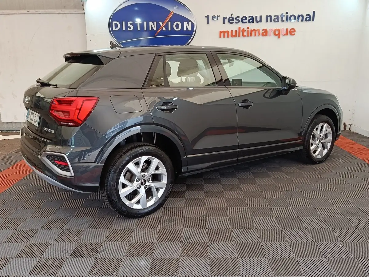 Audi Q2 gris foncé vue de profil côté droit, avec jantes alliage et feux arrière LED visibles en intérieur showroom.