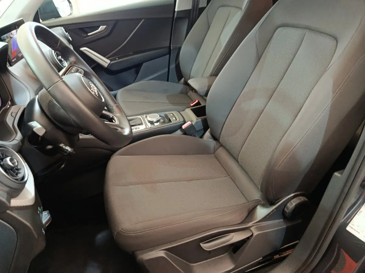 Vue intérieure côté conducteur de l'Audi Q2 35 TFSI 150 S Tronic Business Line 2022 avec sièges tissu gris et volant cuir.