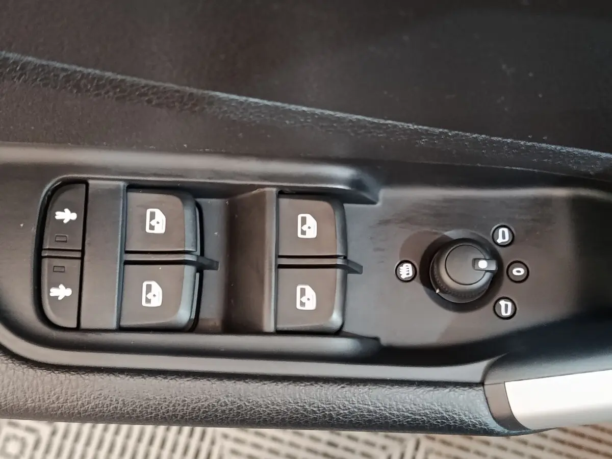Gros plan sur les commandes de lève-vitres et réglage des rétroviseurs côté conducteur de l’Audi Q2 gris foncé 2022.