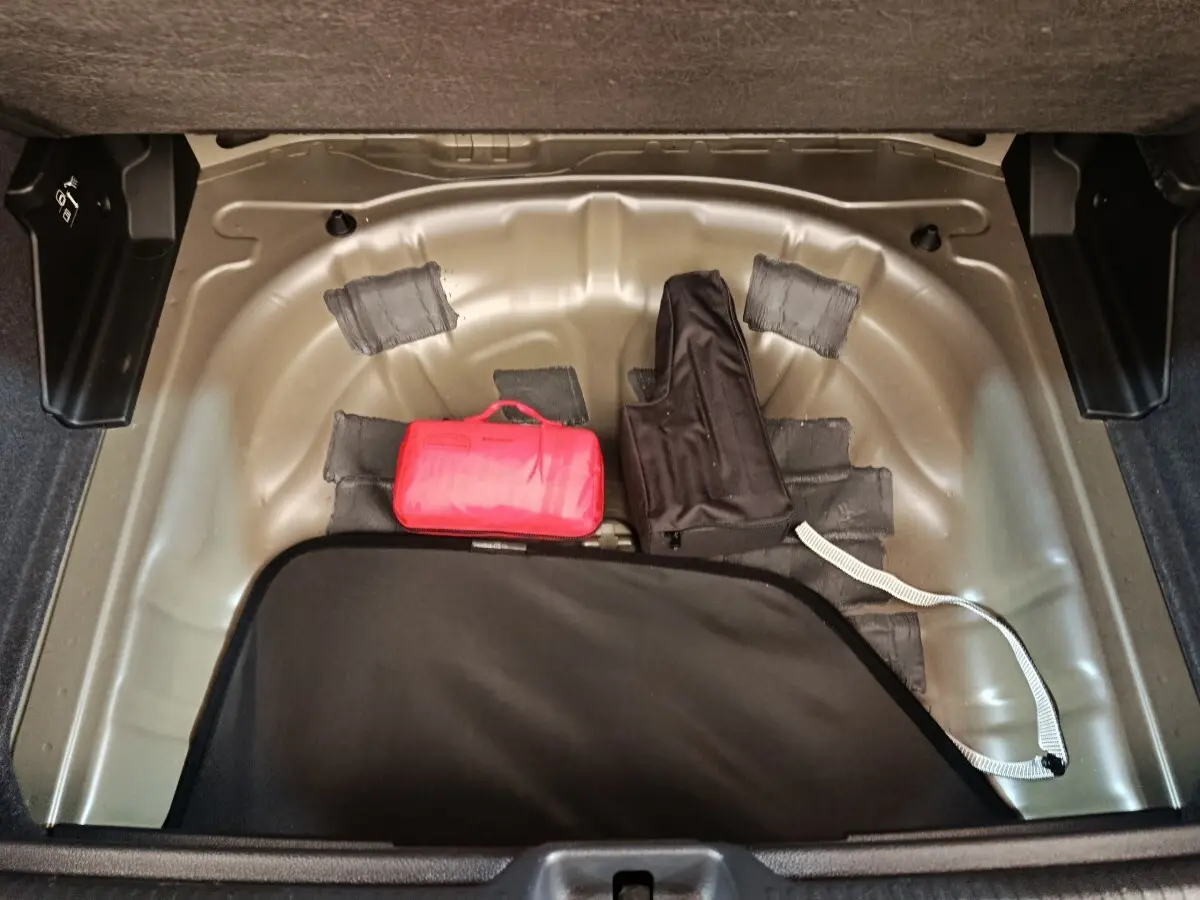 Coffre ouvert d’Audi Q2 gris foncé, vue plongeante sur espace de rangement avec trousse de secours rouge et housse noire.