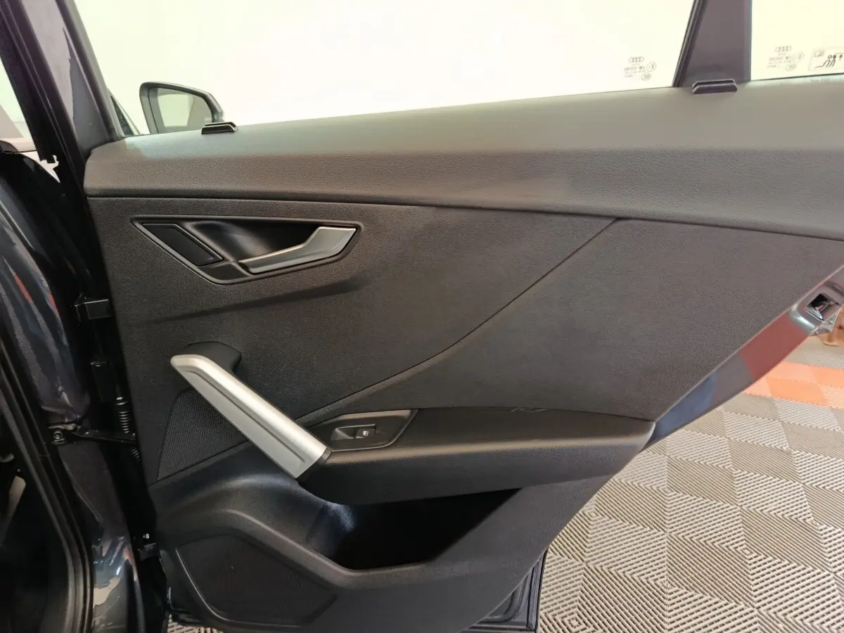 Vue intérieure côté gauche de la porte avant gris foncé de l'Audi Q2 avec poignée argentée et commande de vitre.