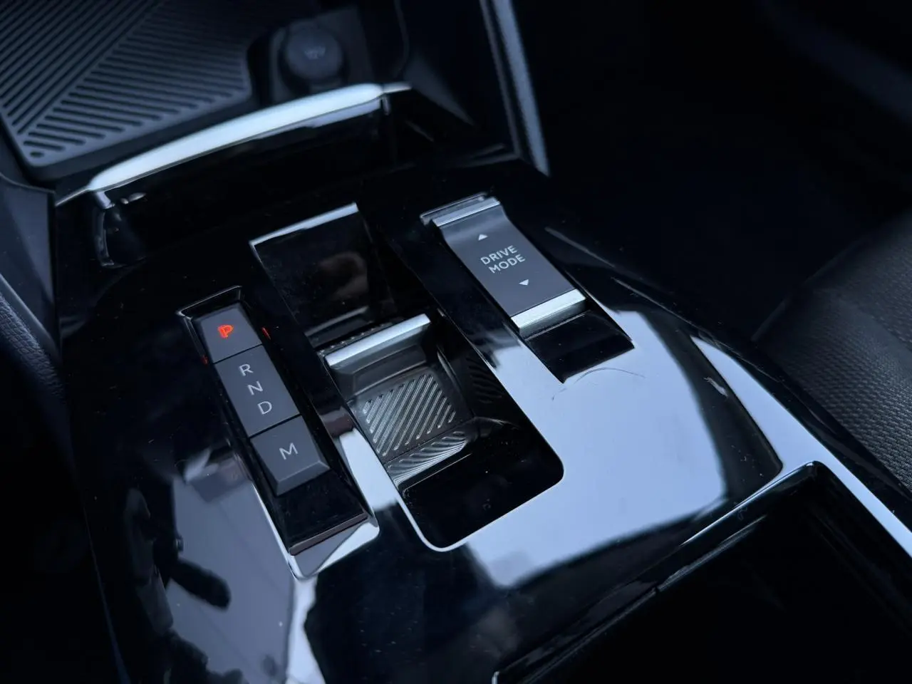 Gros plan sur la console centrale noire brillante de la Citroën C4 Hybrid 2025 avec sélecteur de boîte auto et commande Drive Mode.