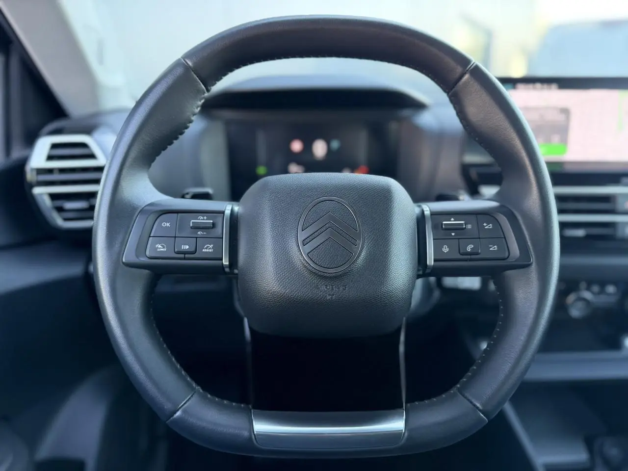 Vue rapprochée du volant en cuir noir de la Citroën C4 Hybrid 145, avec commandes intégrées et tableau de bord flou.