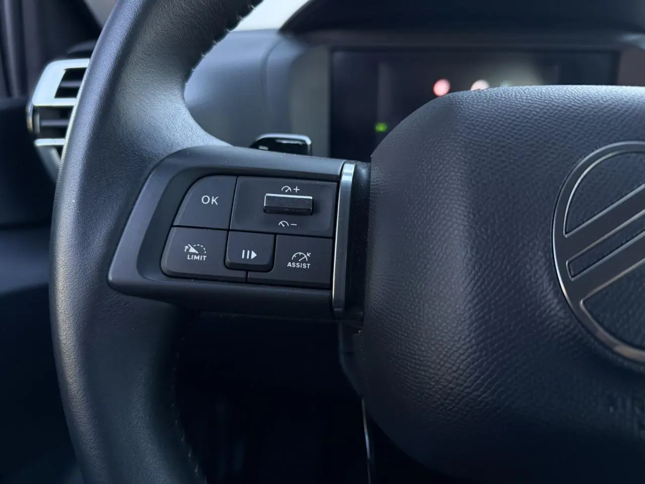 Gros plan sur le volant noir de la Citroën C4 Hybrid 145, avec commandes intégrées côté gauche et logo central.