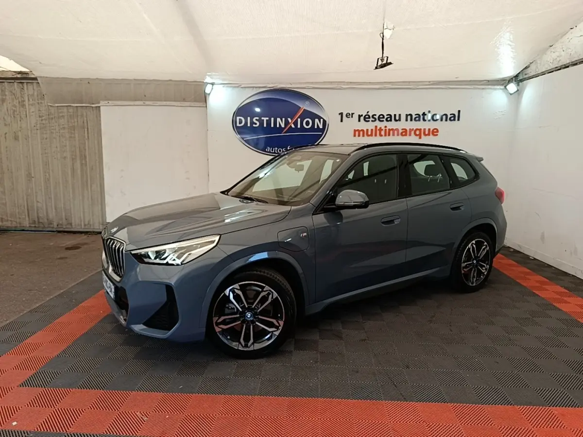 BMW X1 xDrive25e M Sport gris foncé vue 3/4 avant droit en intérieur sur sol noir et rouge.