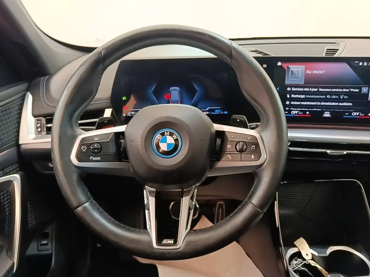 Vue rapprochée du volant cuir et alu multifonctions d’une BMW X1 xDrive25e M Sport 2023, tableau de bord digital visible.