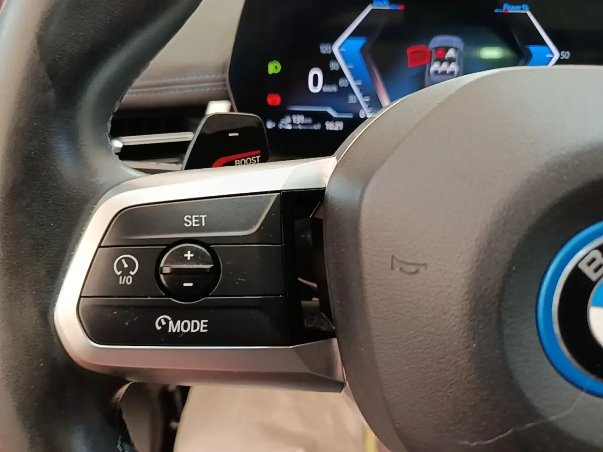 Gros plan sur le volant alu et cuir gris foncé du BMW X1 xDrive25e M Sport avec commandes multifonctions et affichage digital en arrière-plan.