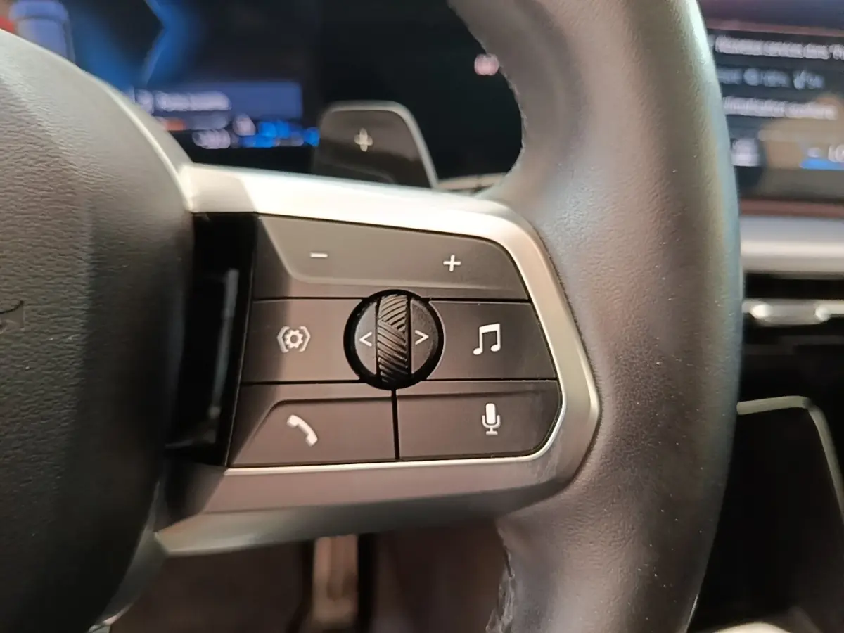 Gros plan sur le volant multifonctions en cuir et alu du BMW X1 xDrive25e M Sport 2023, boutons de contrôle visibles.