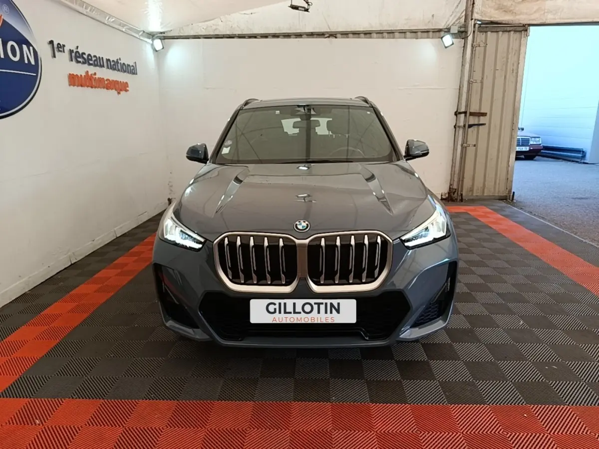 Vue frontale d'un BMW X1 xDrive25e M Sport gris foncé avec calandre imposante et phares LED allumés dans un garage.