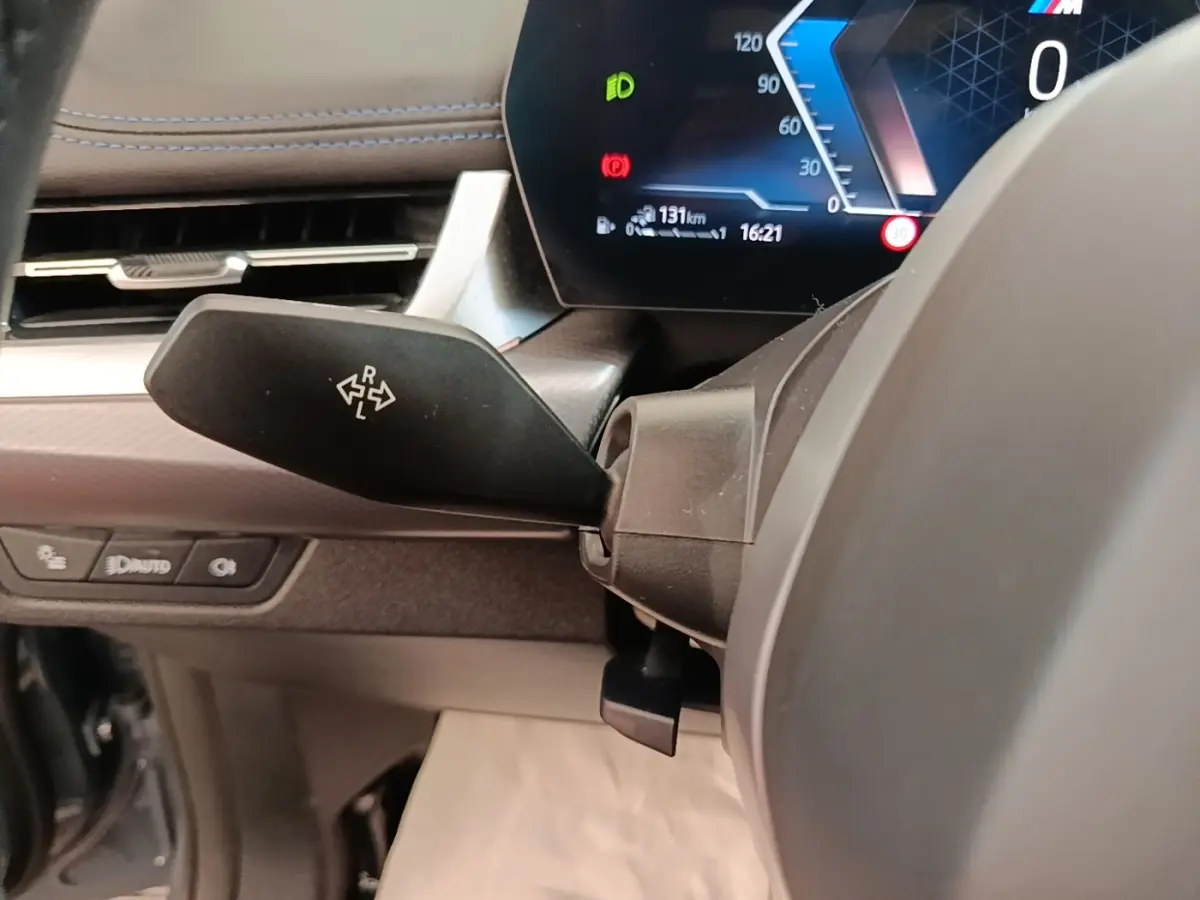 Gros plan sur le commodo de clignotant à gauche du volant cuir alu, tableau de bord digital d'une BMW X1 xDrive25e M Sport gris foncé 2023.