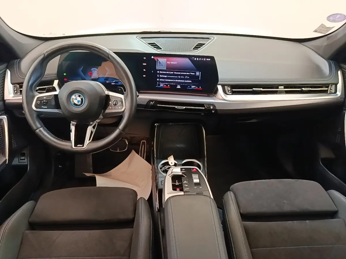Intérieur BMW X1 xDrive25e M Sport 2023 vu de face, volant cuir alu, écran tactile large, sièges noirs en alcantara.