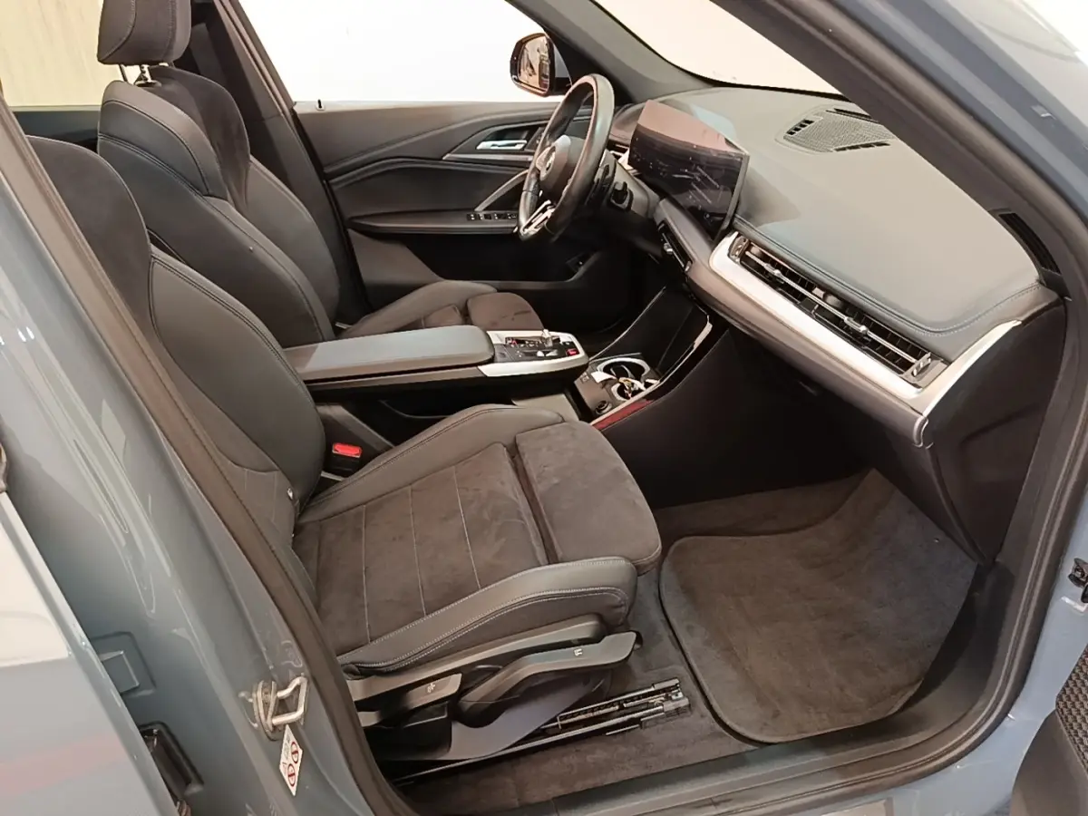 Intérieur côté conducteur BMW X1 xDrive25e M Sport 2023, sièges gris foncé et tableau de bord moderne avec écran tactile.
