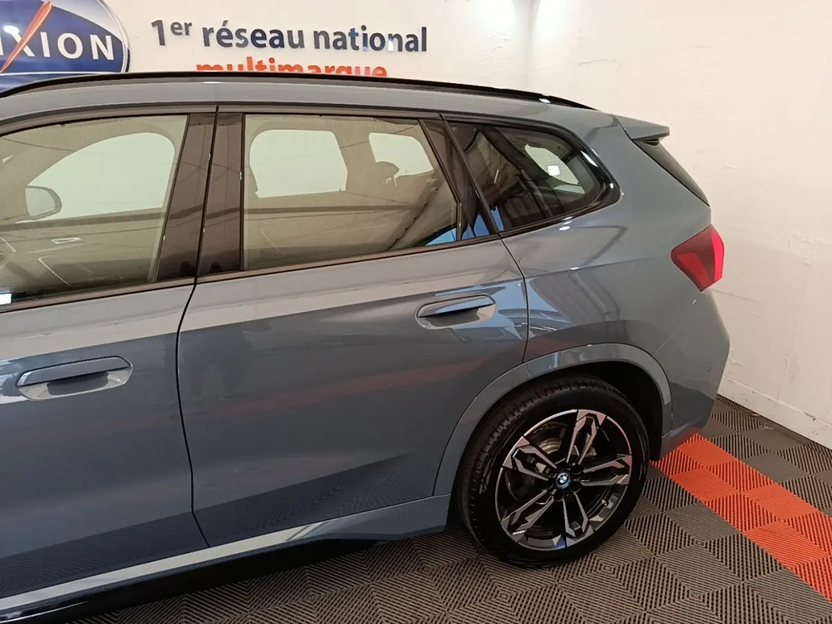Vue latérale droite d’un BMW X1 xDrive25e M Sport gris foncé avec jantes noires et toit noir dans un showroom.