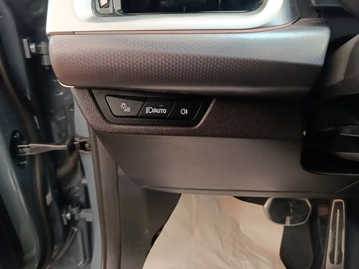 Détail des commandes d’éclairage sur le côté gauche du tableau de bord d’un BMW X1 gris foncé 2023.