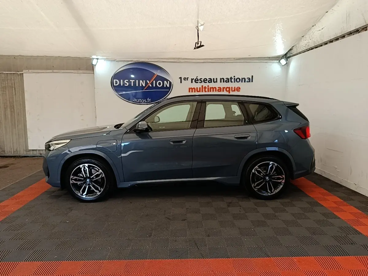 Vue de profil côté gauche d’un BMW X1 xDrive25e M Sport gris foncé, avec jantes alliage et prises de recharge visibles.