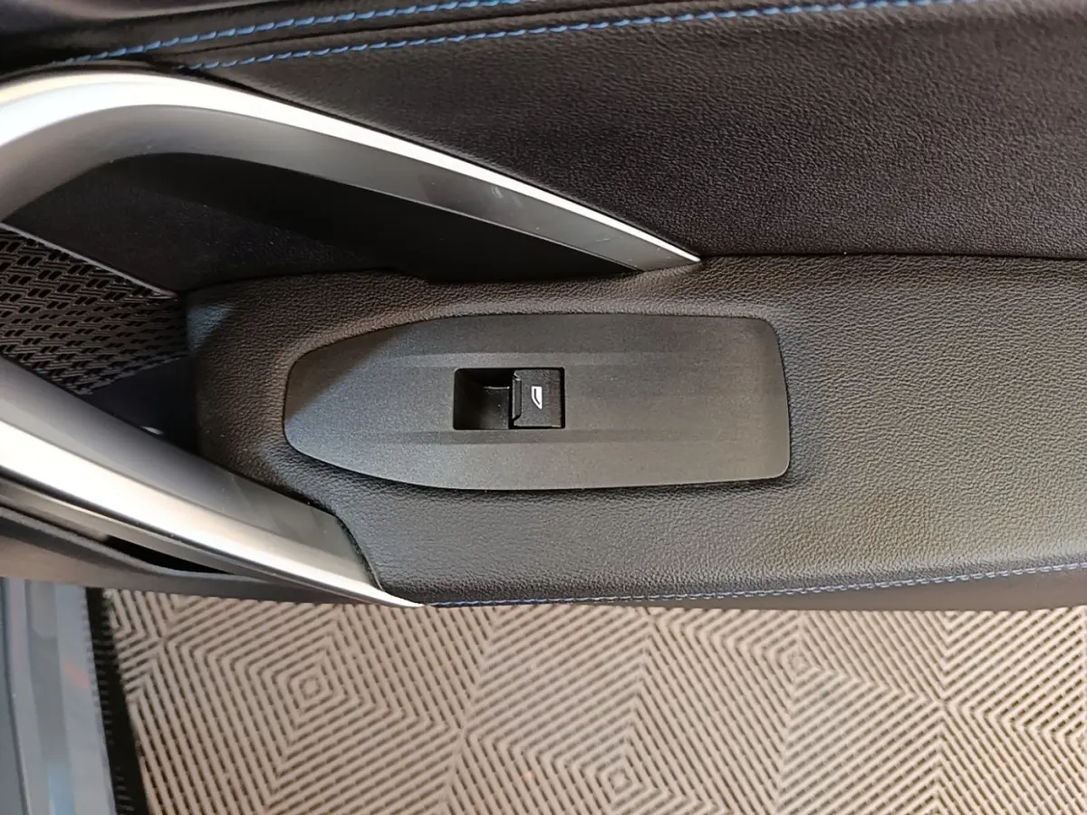 Bouton de commande de lève-vitre sur la porte intérieure côté conducteur d'une BMW X1 gris foncé 2023.