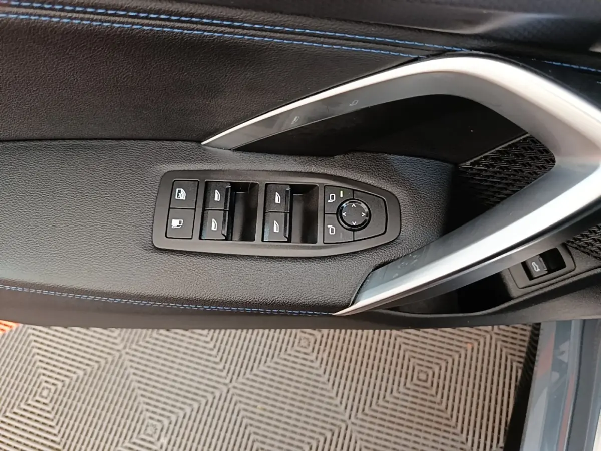 Vue rapprochée de la porte côté conducteur du BMW X1 gris foncé, avec commandes des vitres et rétroviseurs intégrées.