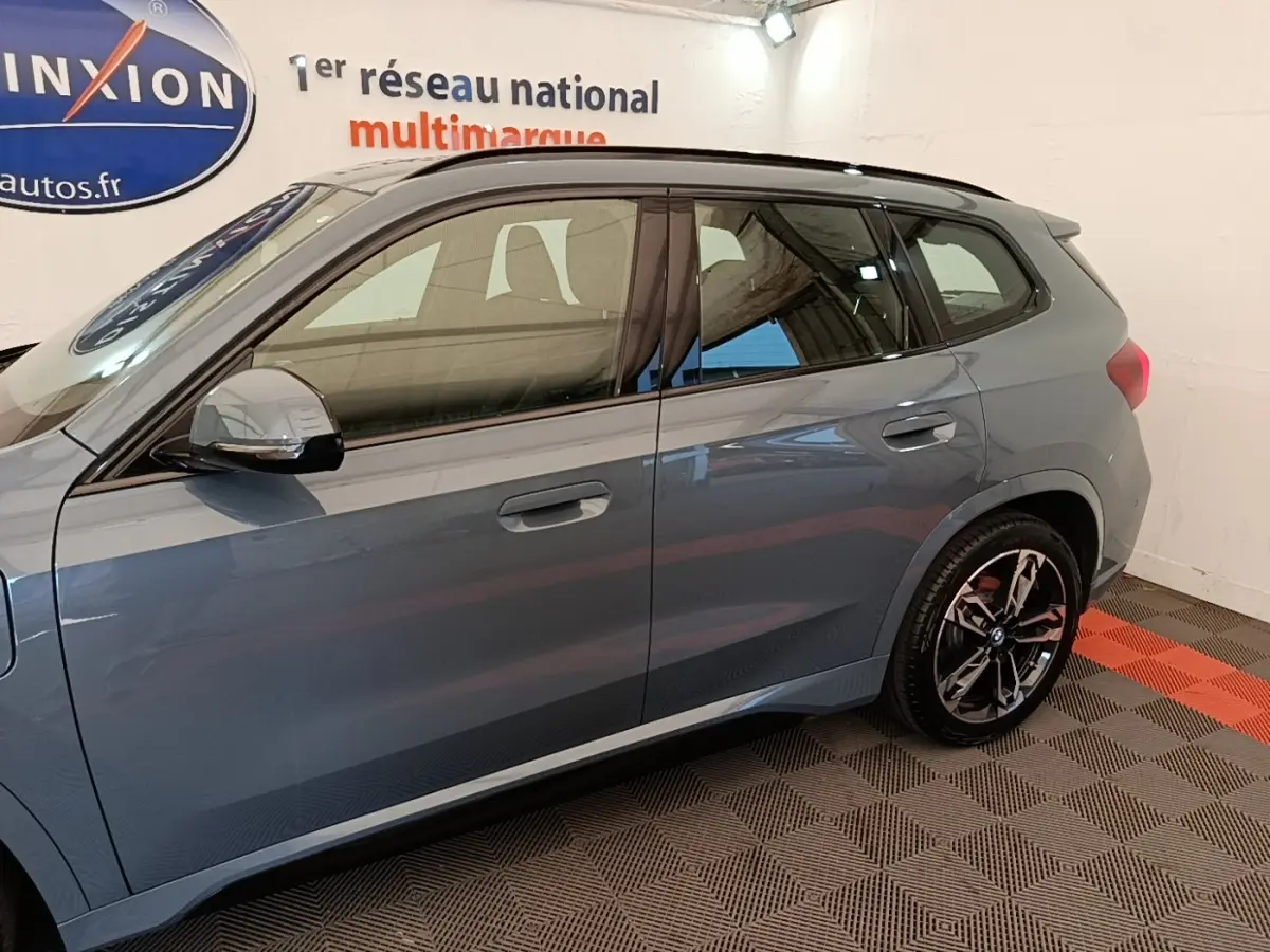 Vue latérale droite d’un BMW X1 xDrive25e M Sport gris foncé avec jantes noires et toit noir en intérieur showroom.