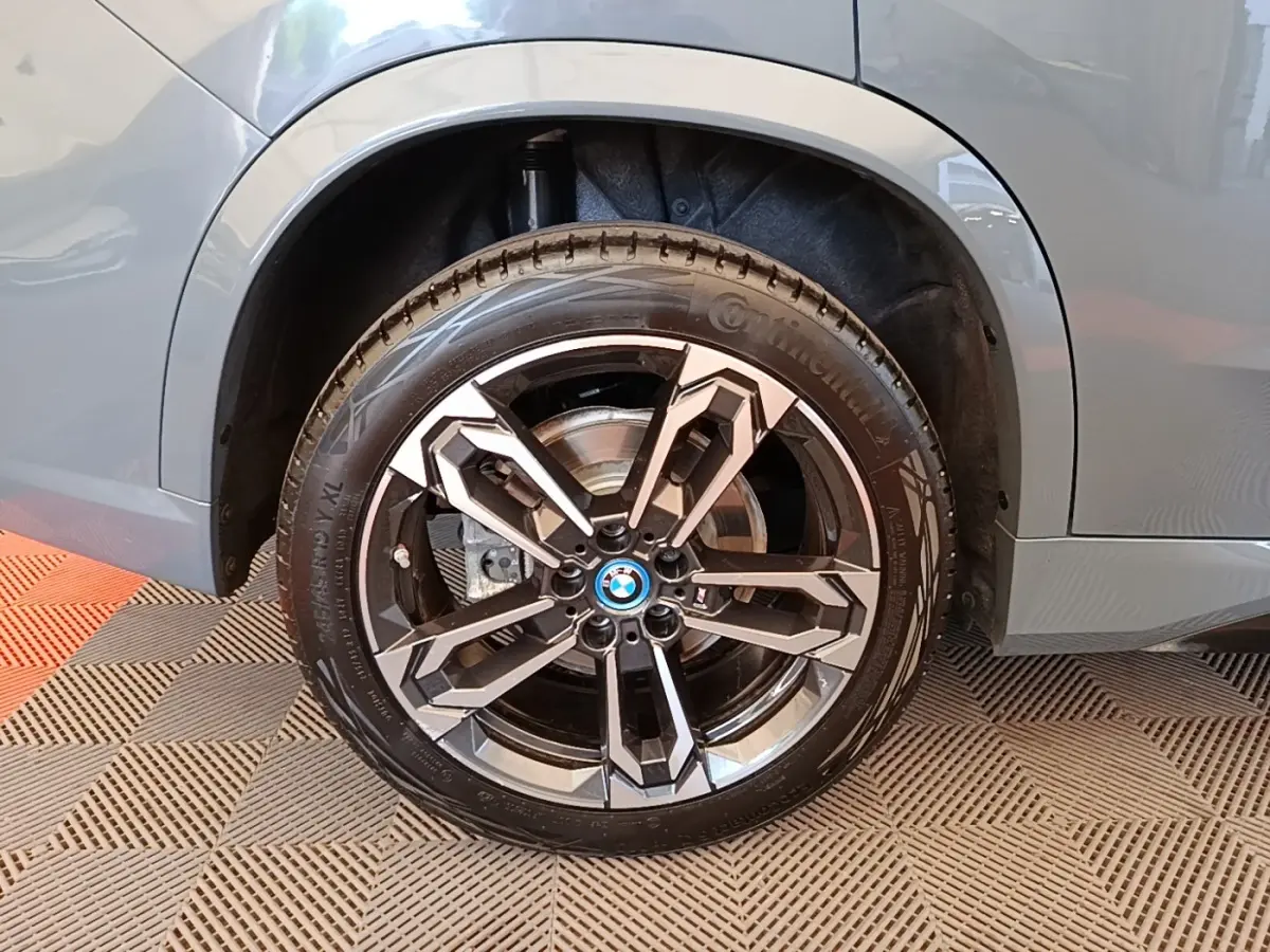 Gros plan sur la roue avant droite d’un BMW X1 gris foncé avec jante alliage au design géométrique.