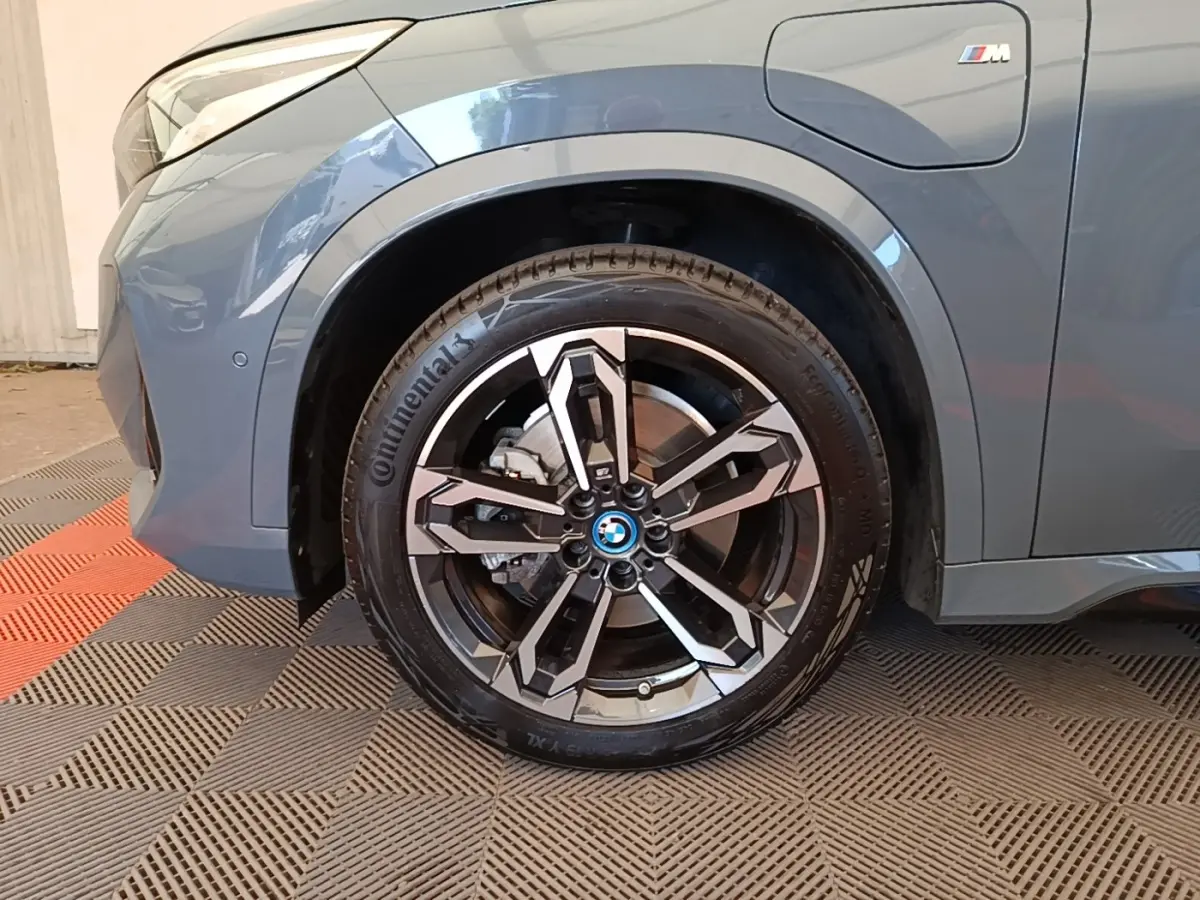 Gros plan sur la roue avant gauche et la partie latérale gris foncé du BMW X1 xDrive25e M Sport avec logo M visible.