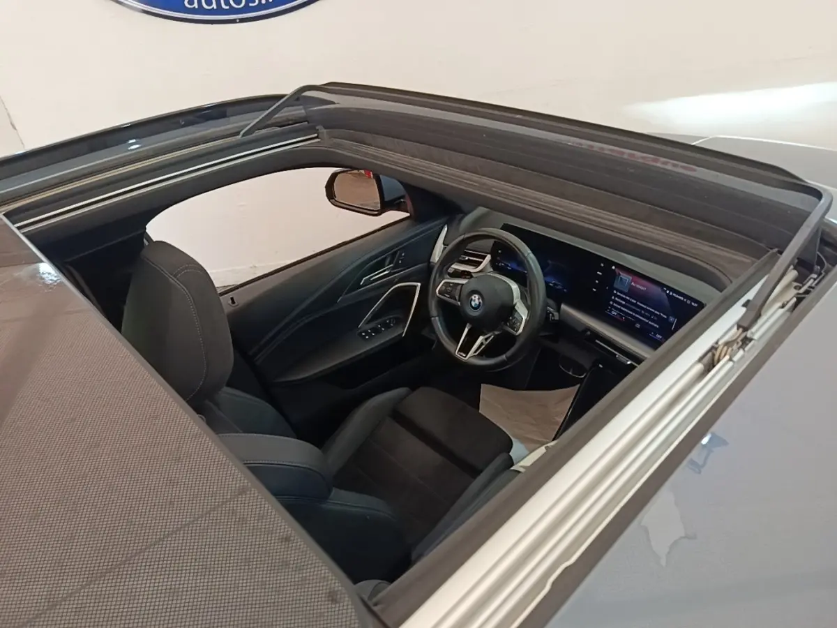 Vue intérieure par le toit ouvrant d'une BMW X1 xDrive25e M Sport gris foncé, volant multifonctions et écran tactile visible.