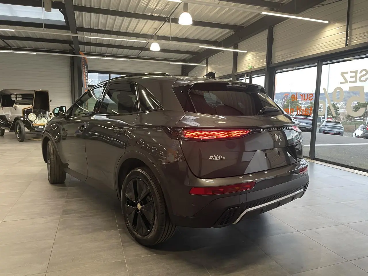 Vue 3/4 arrière droite du DS7 Crossback gris titanium avec feux arrière LED allumés en showroom.