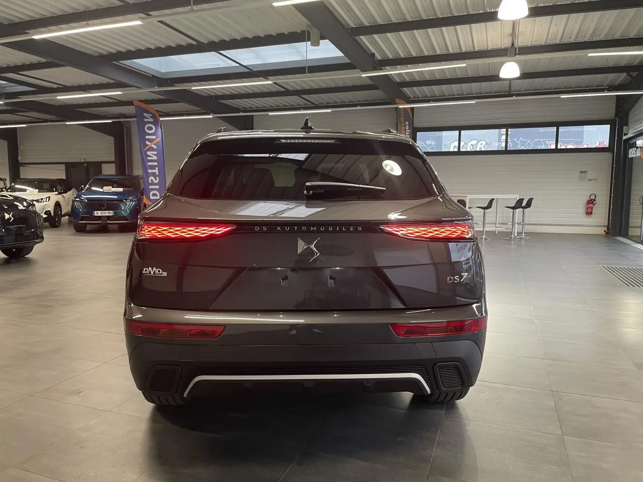 Vue arrière du DS7 Crossback gris titanium avec feux arrière LED 3D et logo DS Automobiles lumineux dans un showroom.