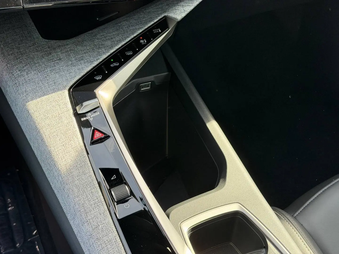 Détail de la console centrale du Peugeot 3008 2026, avec accoudoir tissu gris et commandes noires brillantes.