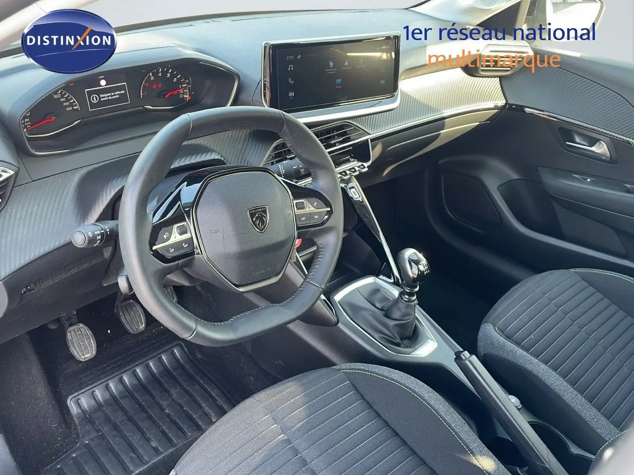 Vue intérieure côté conducteur de la Peugeot 208 1.2 PureTech 100ch Active 2024 avec volant compact et levier de vitesse manuel.