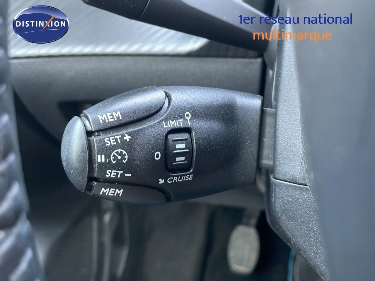 Gros plan sur la commande de régulateur de vitesse noire à gauche du volant dans un Peugeot 208 blanc banquise 2024.