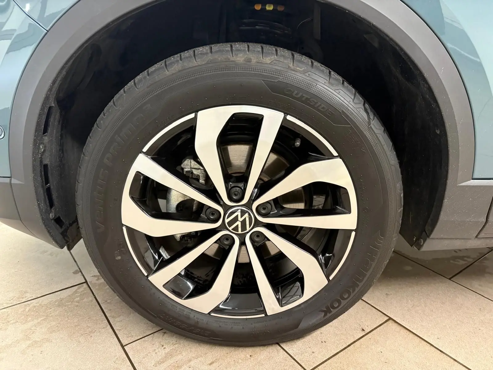 Gros plan sur la roue avant gauche du Volkswagen T-Roc bleu pétrole, mettant en valeur la jante alliage bicolore au design moderne.