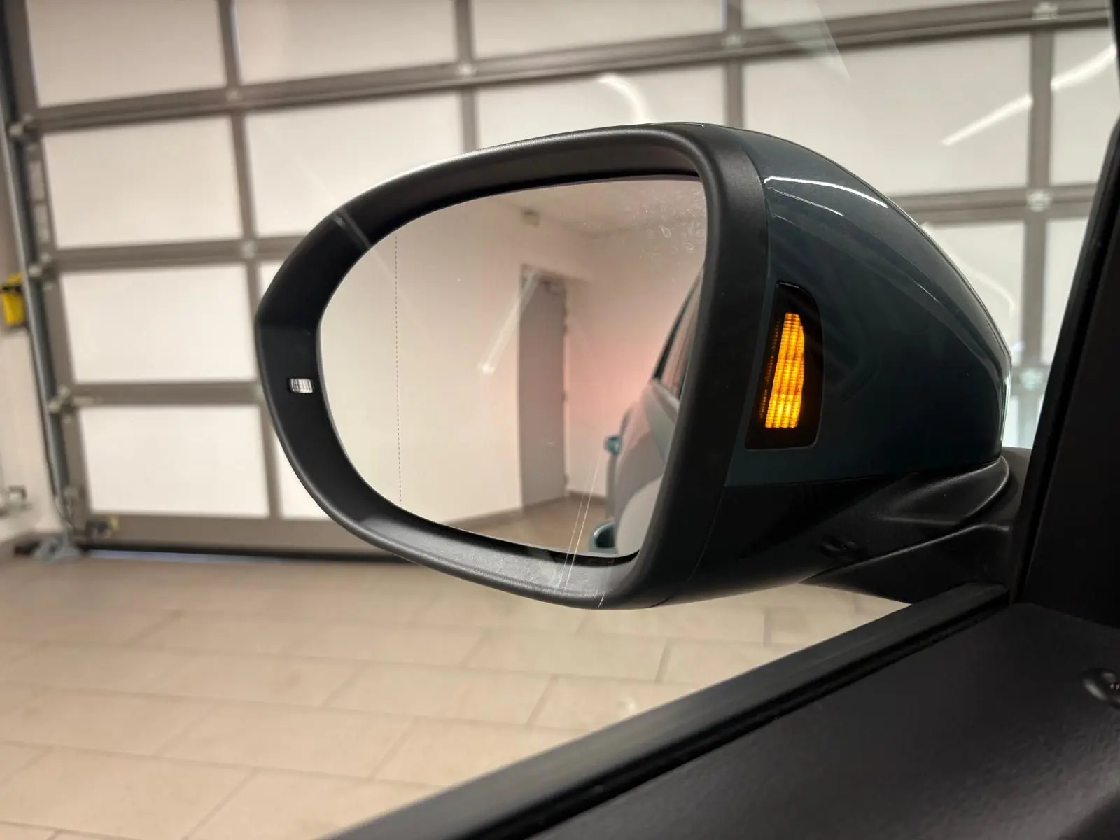 Rétroviseur extérieur droit du Volkswagen T-Roc bleu pétrole 2025 avec clignotant orange allumé en intérieur.