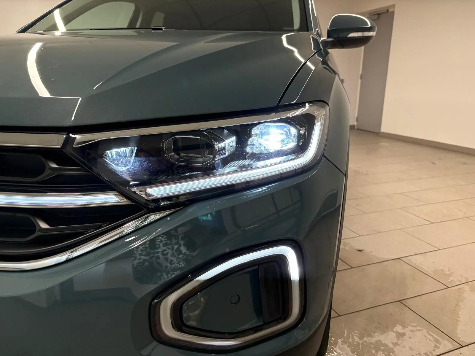 Gros plan sur l'avant droit du Volkswagen T-Roc bleu pétrole 2025, mettant en valeur le phare LED allumé et la calandre.