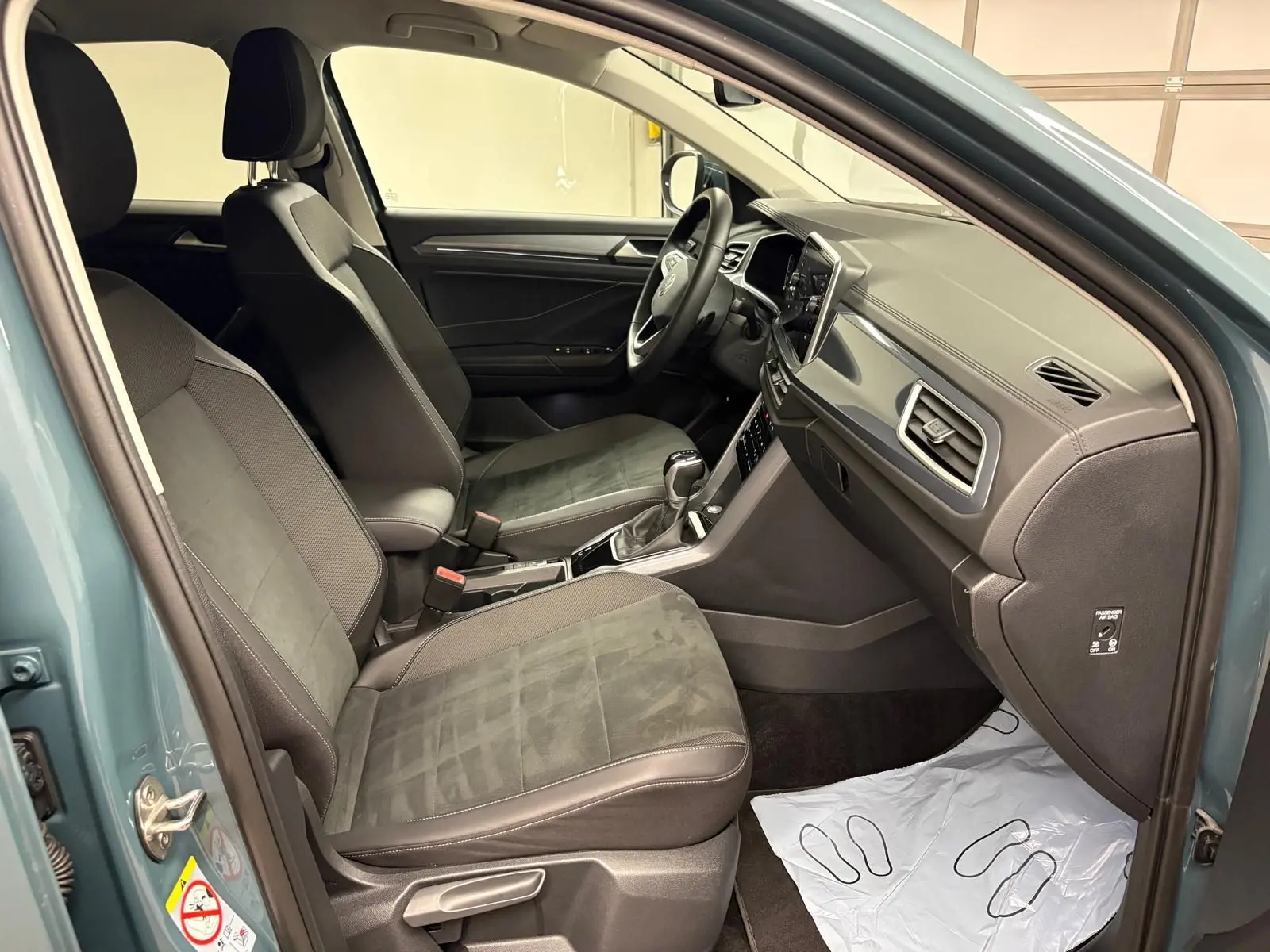 Vue intérieure côté conducteur du Volkswagen T-Roc 1.5 TSI bleu pétrole, mettant en valeur les sièges et le tableau de bord.