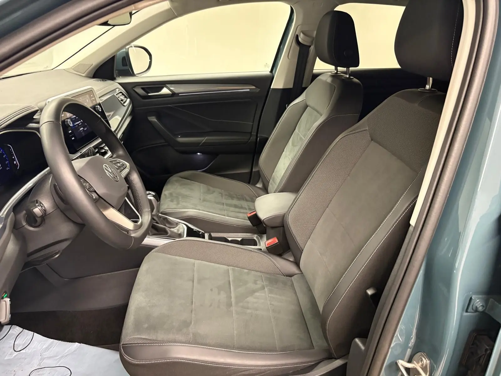 Vue intérieure côté conducteur du Volkswagen T-Roc 2025 bleu pétrole, sièges avant en tissu et volant multifonction.
