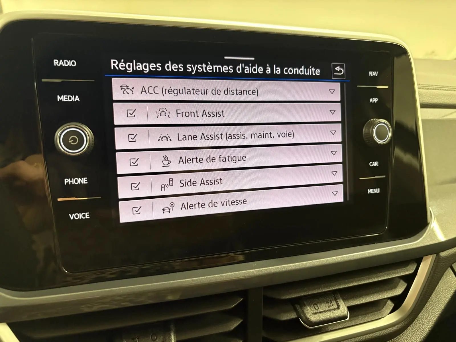 Écran tactile central du Volkswagen T-Roc 2025 affichant les réglages des aides à la conduite, avec commandes autour de l'écran.