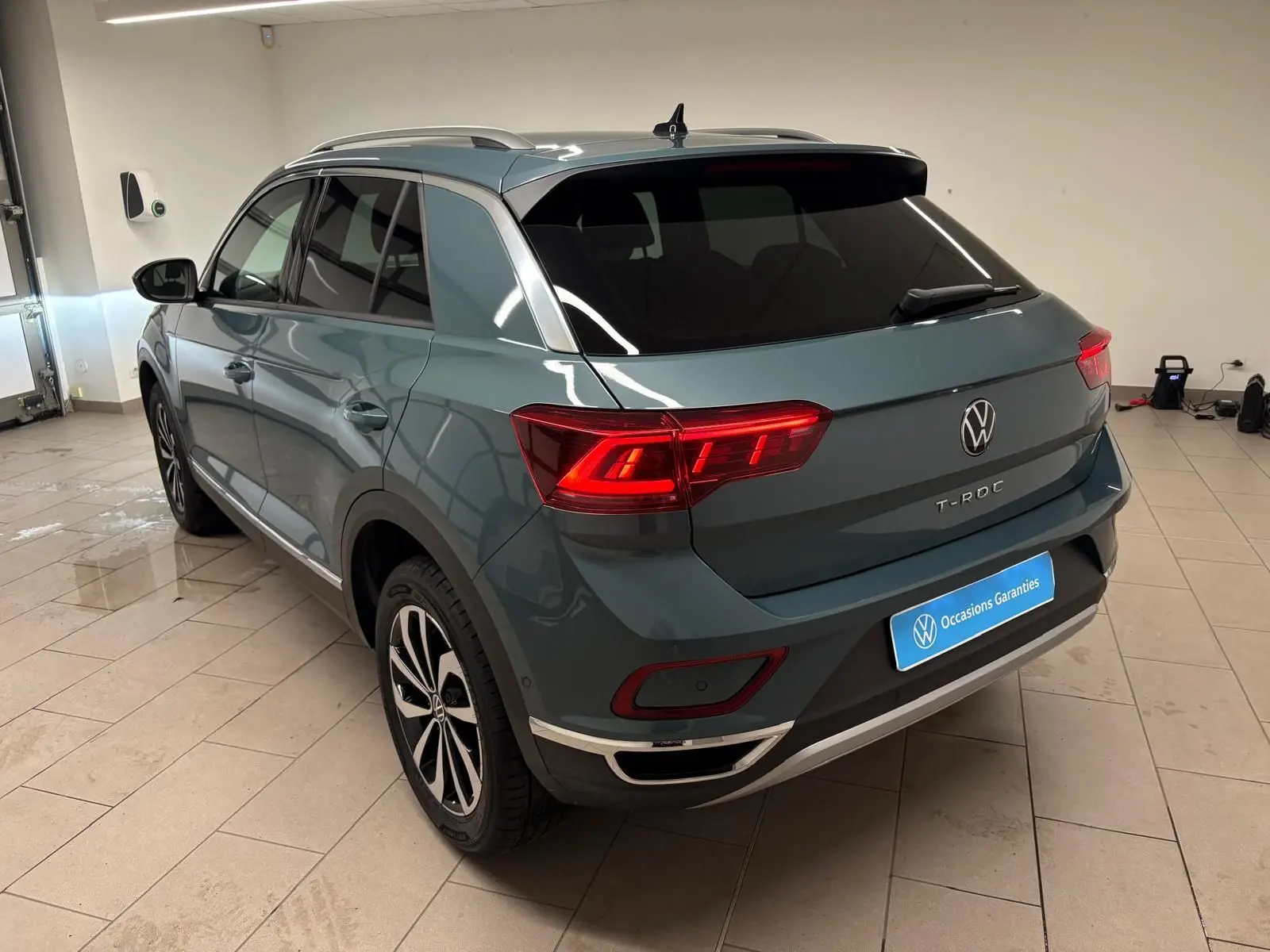Vue 3/4 arrière droite d’un Volkswagen T-Roc 1.5 TSI 150 DSG7 Style Edition bleu pétrole avec feux arrière allumés en intérieur.