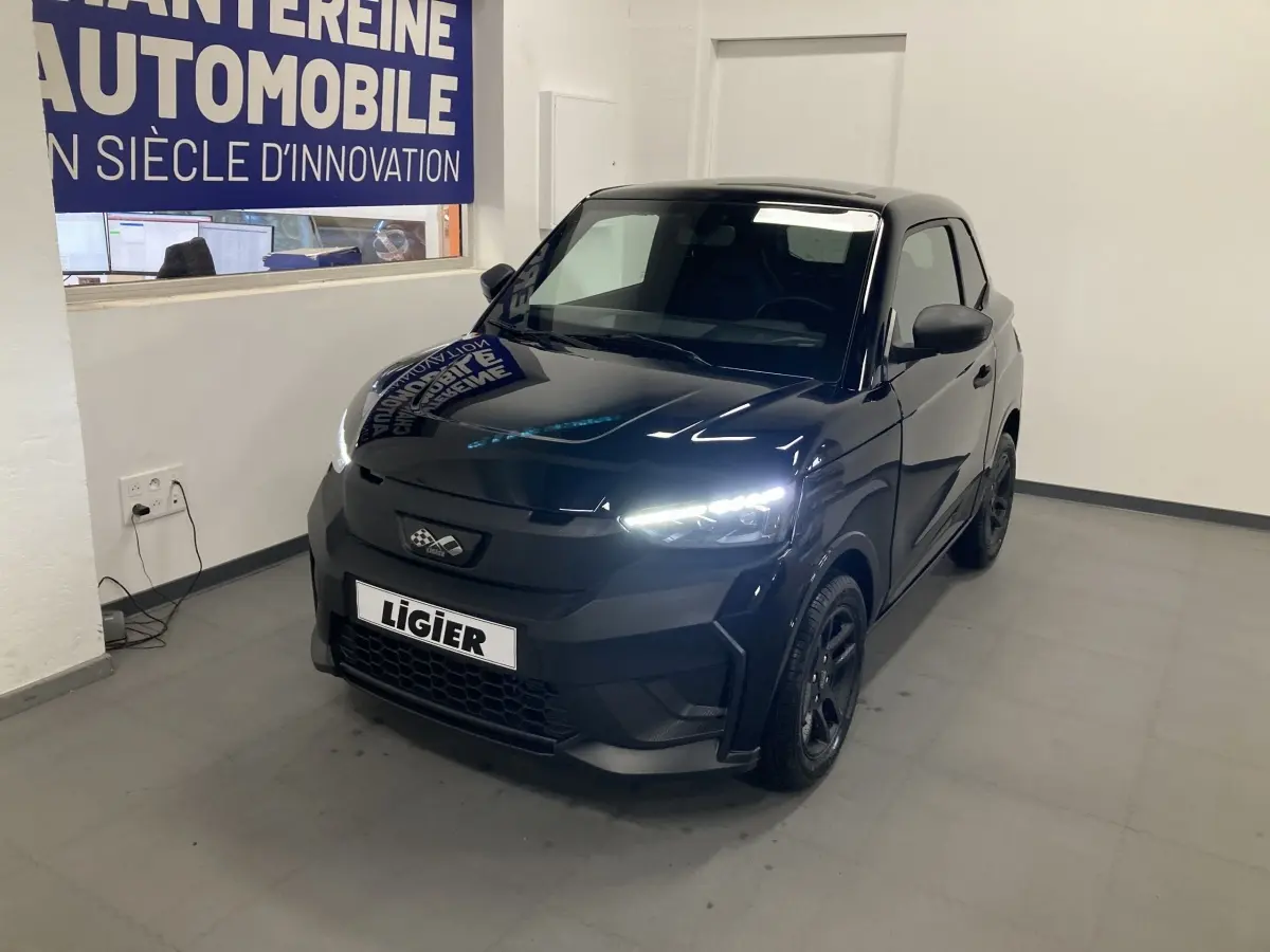 Vue 3/4 avant d'une Ligier JS50 noire 2026 avec feux LED allumés et jantes alu noires en intérieur showroom.
