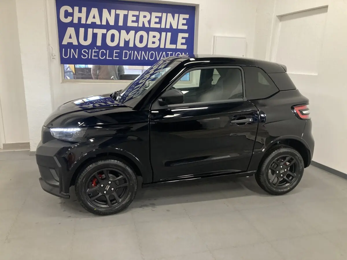 Vue de profil côté gauche d'une LIGIER JS50 0.5 REVO D+ SELECT noire avec jantes alu noires et feux LED en intérieur showroom.