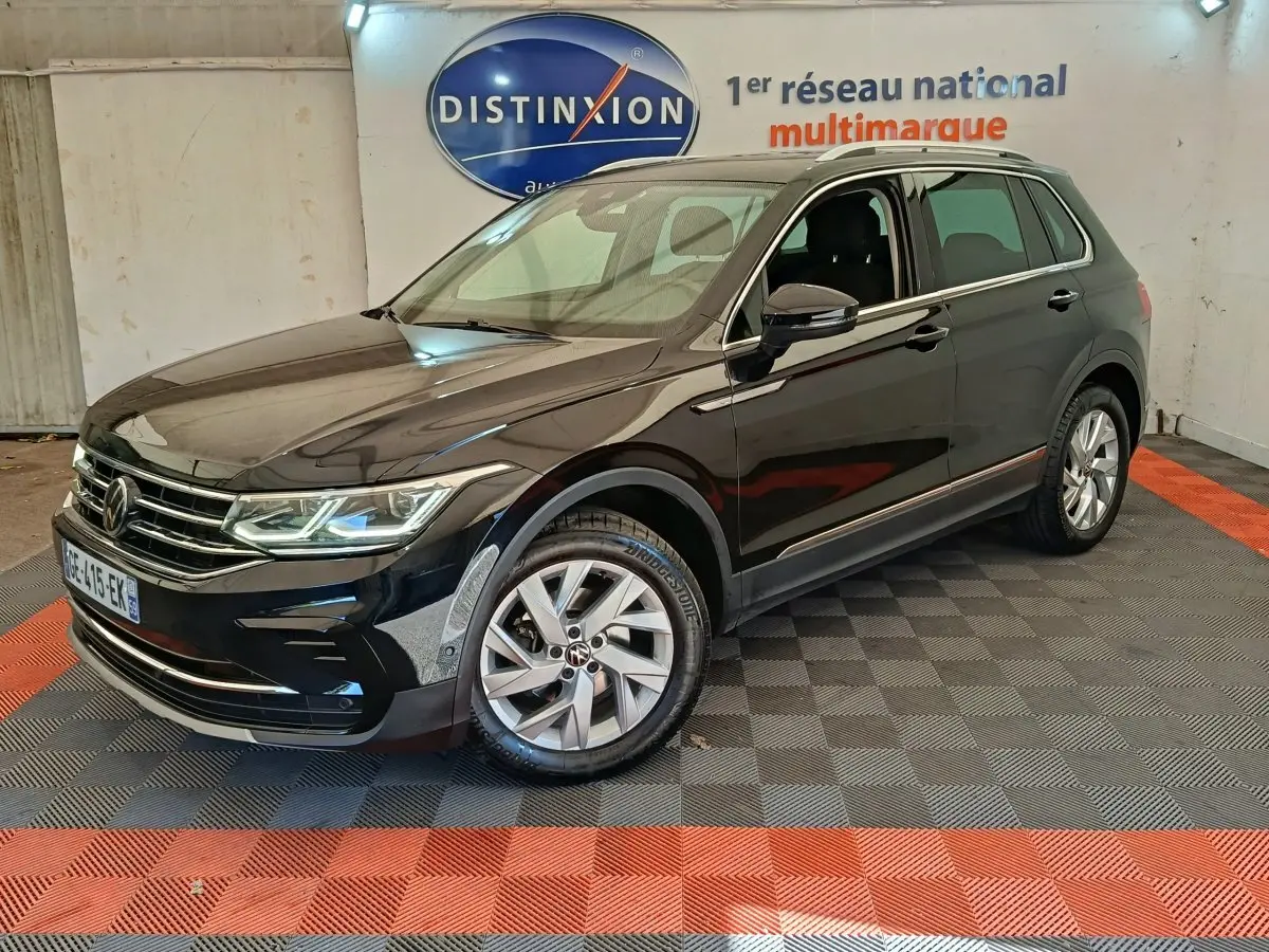 Volkswagen Tiguan noir vu en 3/4 avant droit dans un showroom avec sol à damier gris et rouge.