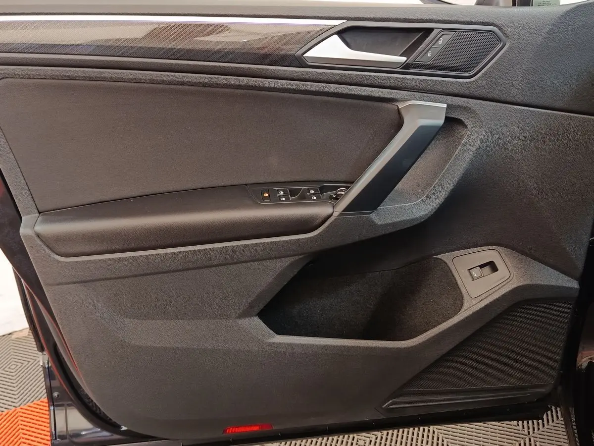 Vue intérieure côté gauche de la porte avant noire du Volkswagen Tiguan 2.0 TDI 150 DSG7 Elegance avec commandes électriques.
