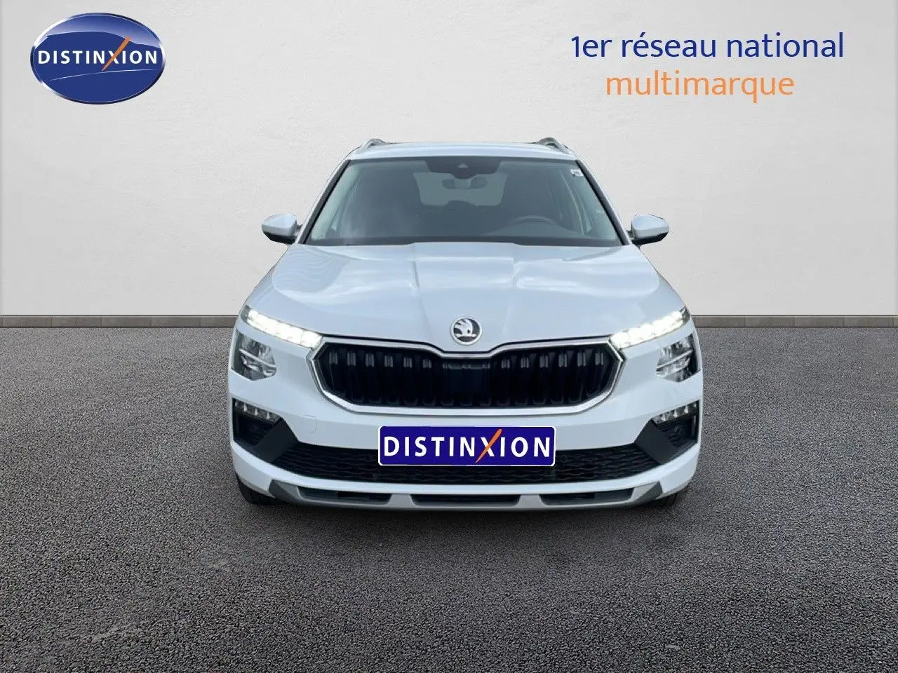 Vue avant d'un Skoda Kamiq blanc glacier 2025 avec calandre noire et feux LED allumés sur fond neutre.
