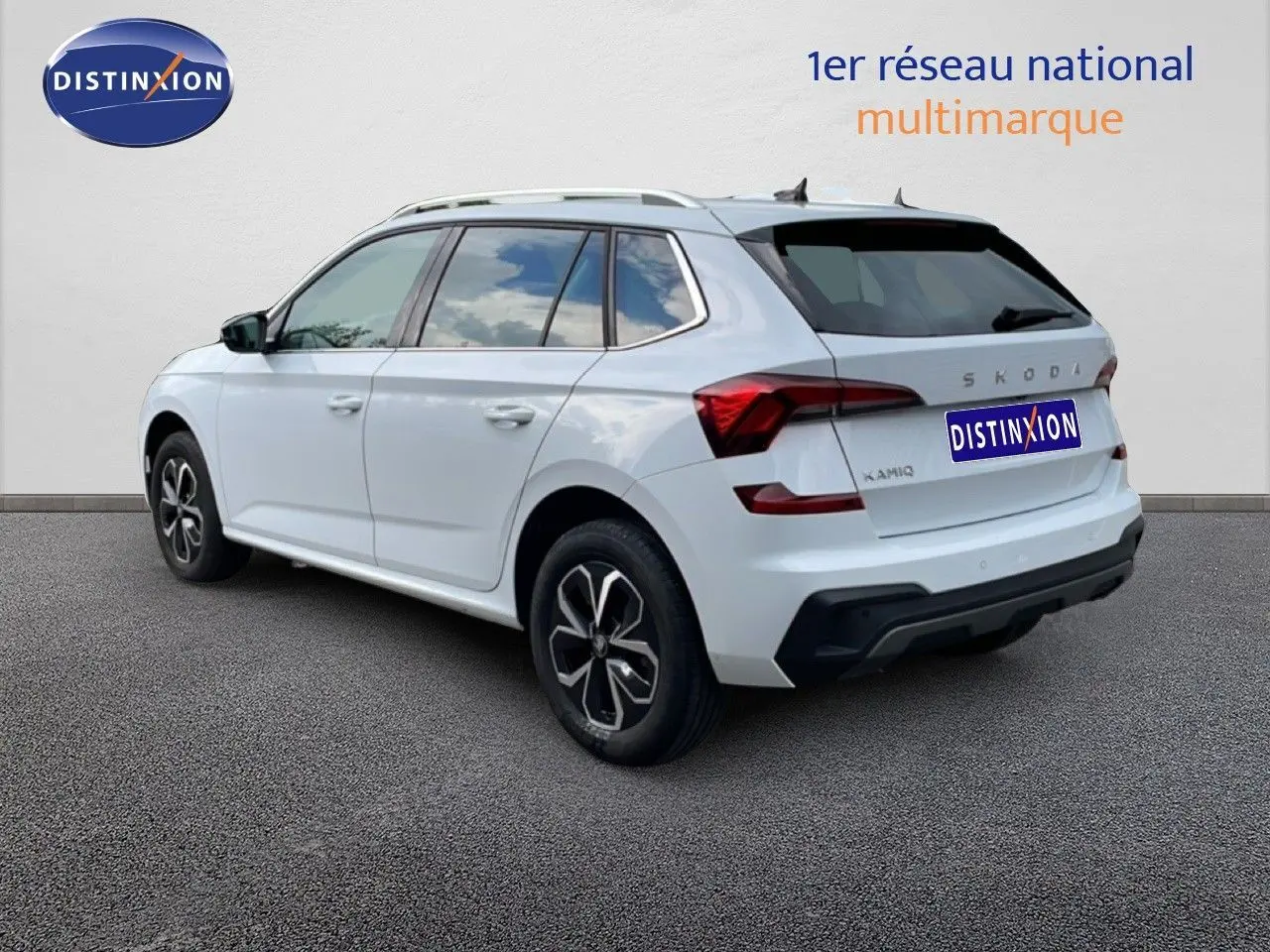 Vue 3/4 arrière droite d'un Skoda Kamiq blanc glacier avec jantes noires et toit ouvrant visible.