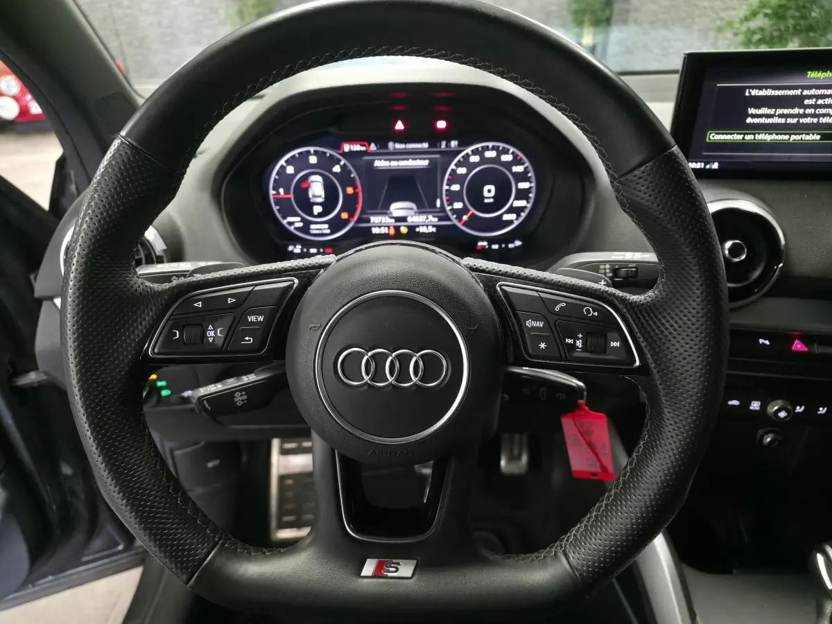 Vue rapprochée du volant sport S line en cuir noir avec méplat et tableau de bord numérique de l'Audi Q2 gris 2023.