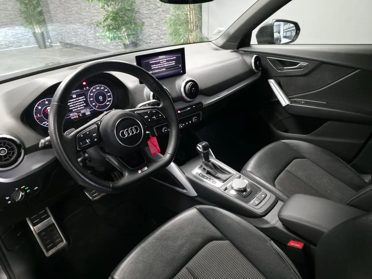 Vue intérieure côté conducteur de l'Audi Q2 S line Plus 2023, avec volant sport cuir noir et console centrale moderne.
