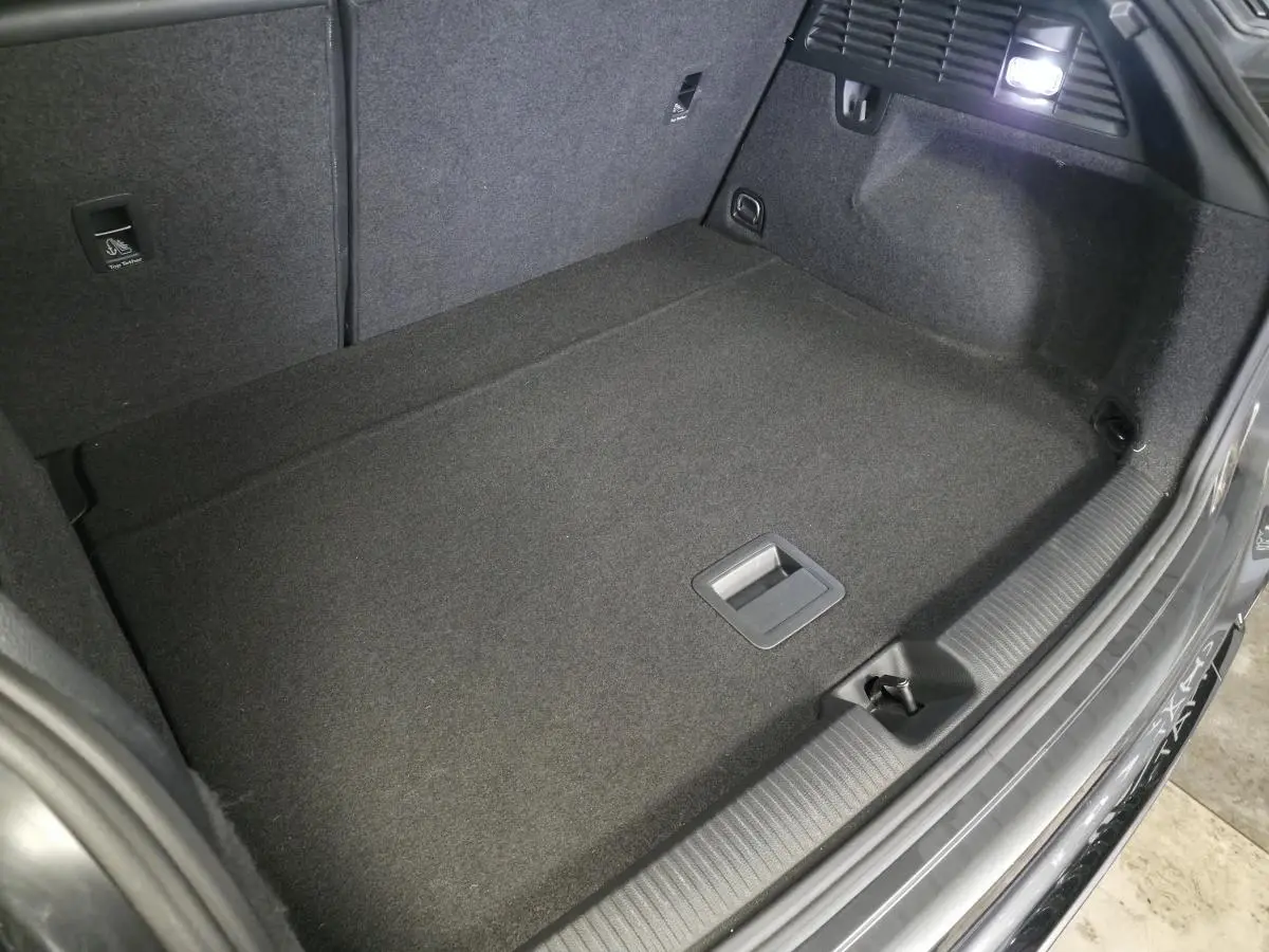 Vue intérieure du coffre spacieux et propre de l'Audi Q2 gris, avec éclairage et revêtement en tissu noir.